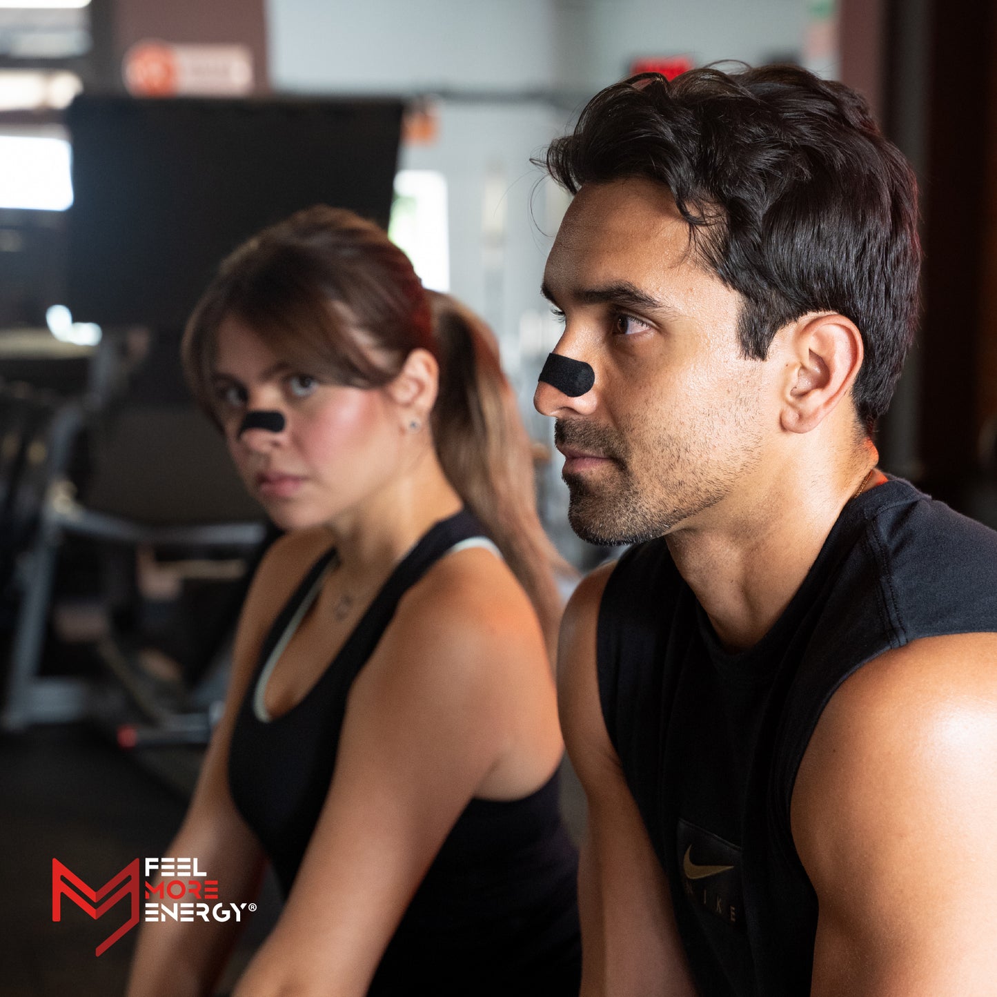 Two people wearing black tank tops with a visible brand logo in a gym setting.