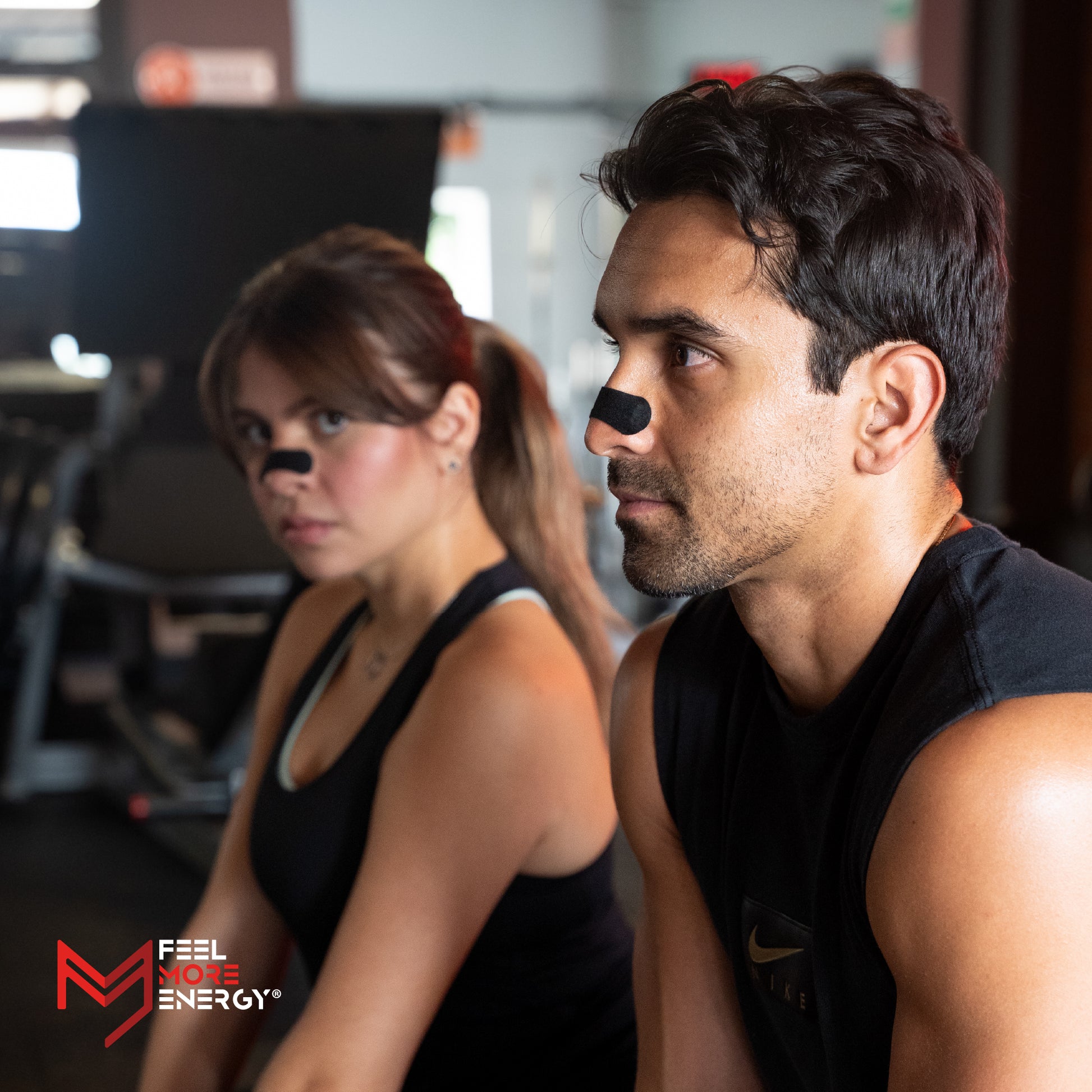 Two people wearing black tank tops with a visible brand logo in a gym setting.