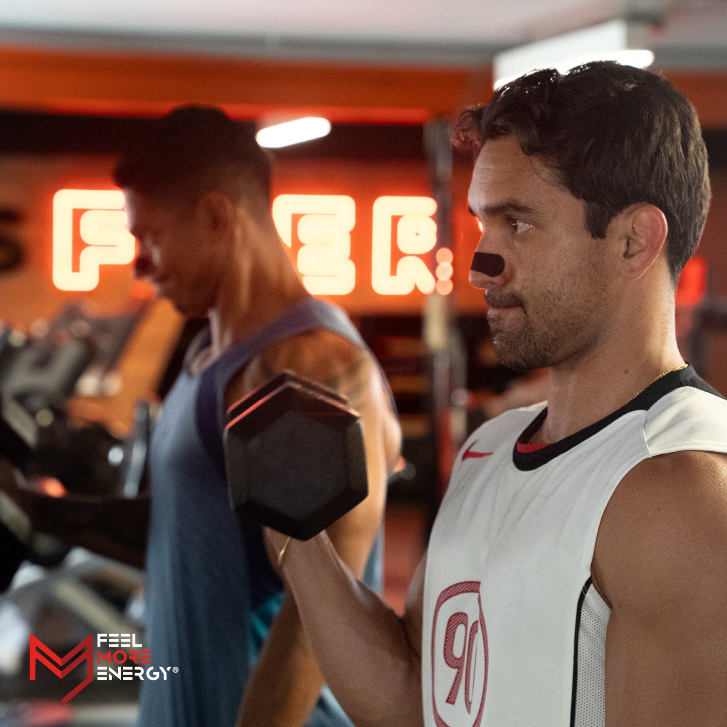 Man lifting a dumbbell in a gym with 'Feel More Energy' branding.