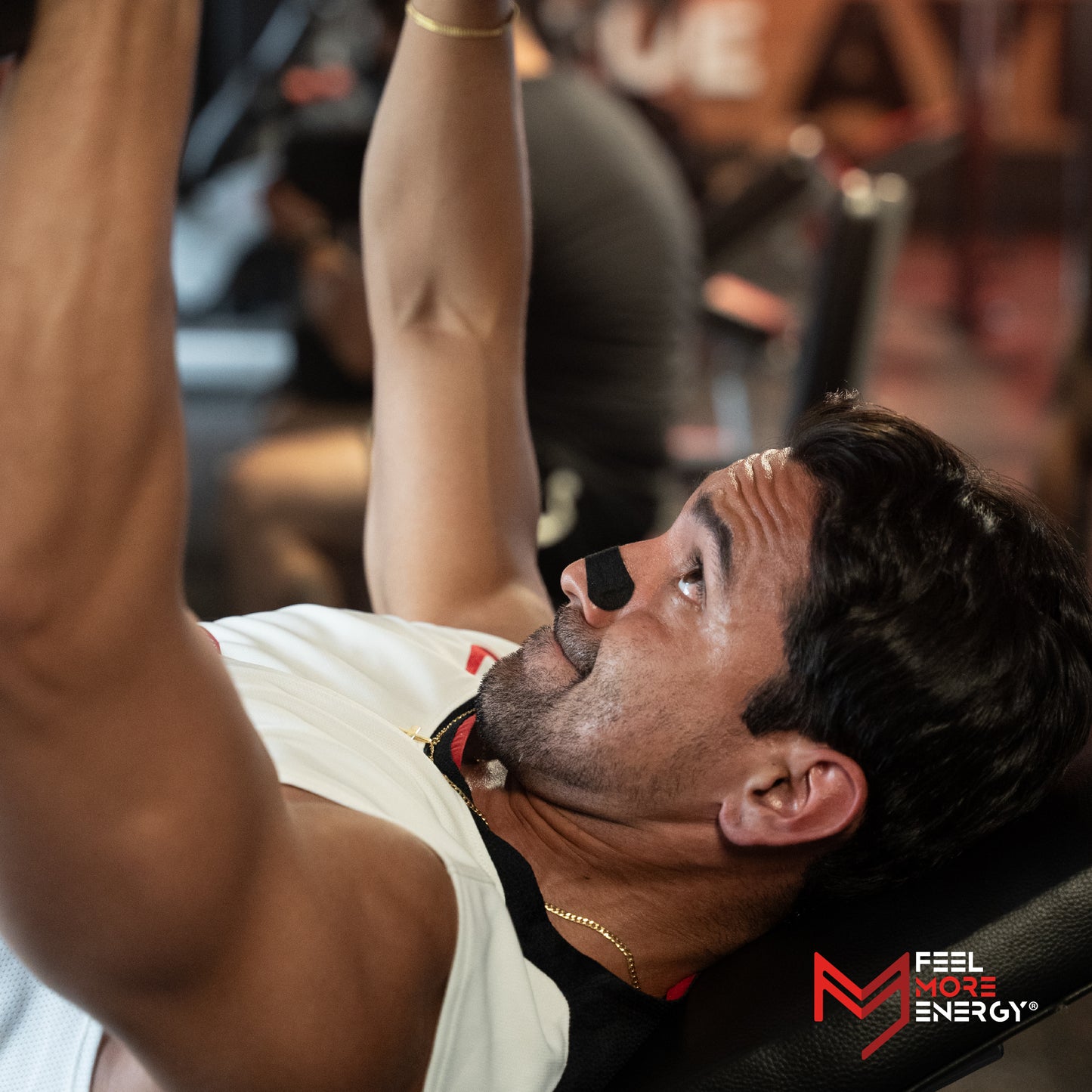 Man performing a bench press in a gym with 'Feel More Energy' branding.